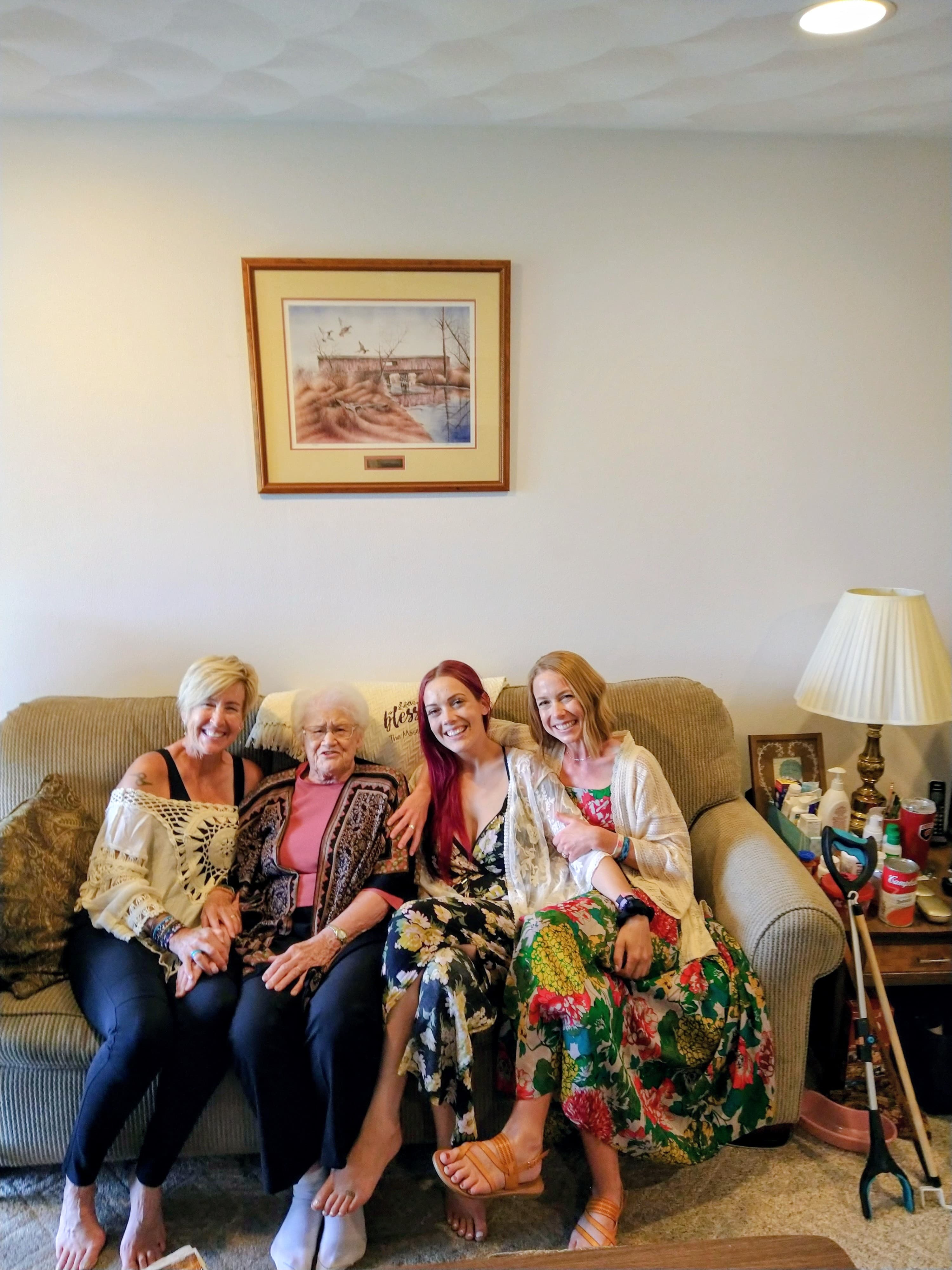 Four women of different generations sit together on a tan couch, smiling for a photo.