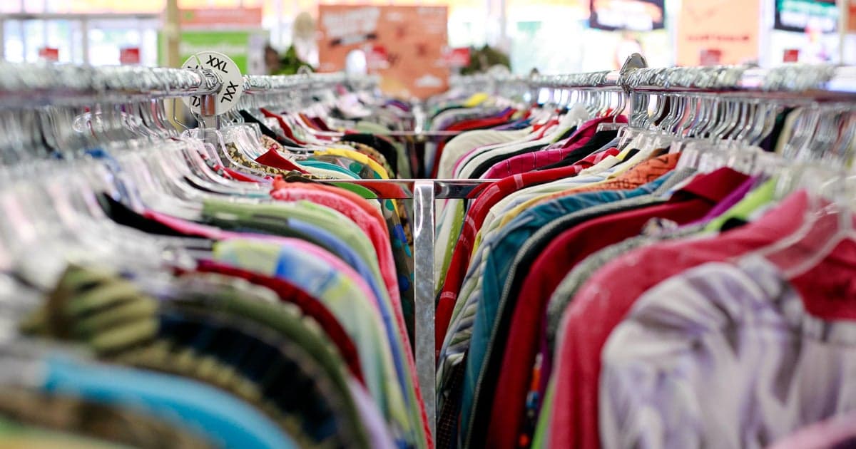 Rows of colorful garments hanging on metal racks in a brightly lit retail store.
